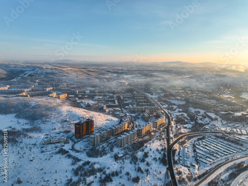 Expansive aerial view of snow-covered Murmansk city, with residential buildings and roads, under a clear sky, Russia