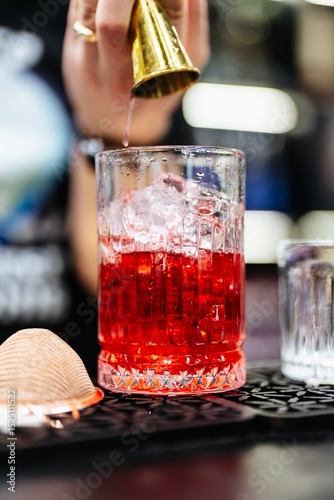 Crafting a vibrant cocktail with precision at a lively bar in the evening