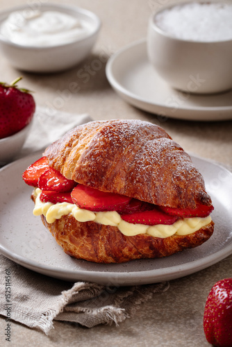 Croissant with strawberries and vanilla cream on plate with coffee and yogurt