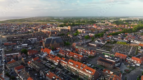 Aerial view of a Dutch town with a prominent church in the center, surrounded by residential homes, green trees, and a clear blue sky on a bright spring day. Peaceful and charming atmosphere.