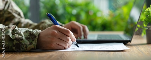 Person writing on paper with laptop nearby