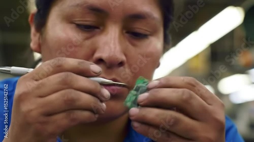 Woman Working Meticulously on Circuit Board Assembly in a Well-Lit Factory Environment
