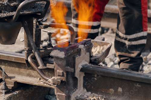 A worker in the process of a railroad track weld repair, reconstruction with a freight train passing