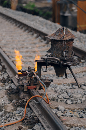 A worker in the process of a railroad track weld repair, reconstruction with a freight train passing