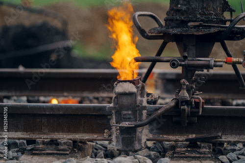 A worker in the process of a railroad track weld repair, reconstruction with a freight train passing