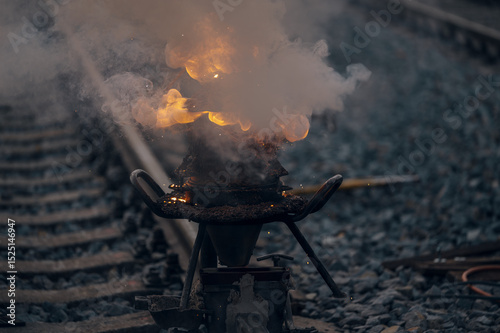 A worker in the process of a railroad track weld repair, reconstruction with a freight train passing