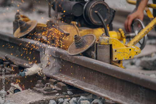 A worker in the process of a railroad track weld repair, reconstruction with a freight train passing