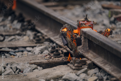 A worker in the process of a railroad track weld repair, reconstruction with a freight train passing