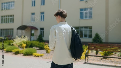 Rear view of young student with backpack arriving at a modern school