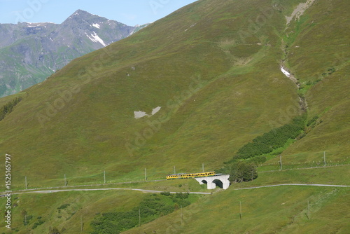 a yellow train crossing grand mountains, Switzerland