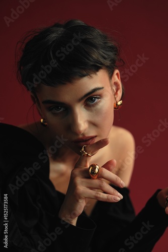 Elegant woman poses with bold jewelry against a rich backdrop while conveying a sense of intrigue and allure through her expression