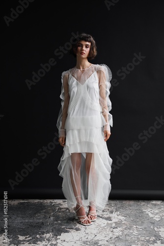 Elegant model showcasing a stunning white dress in a modern studio setting, highlighting intricate design details against a dark backdrop