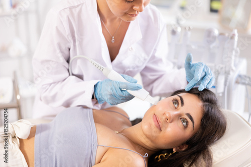 Young female patient receiving facial skin cleansing with ultrasonic shovel to enhance efficacy of skincare products and improving skin texture. Modern hardware cosmetology