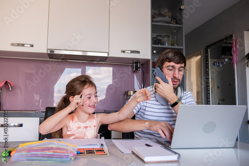 Father is trying to work from his laptop while talking on the phone and his daughter is disturbing him while drawing and painting at the kitchen table