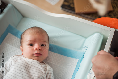 Parent preparing to change the diaper of a newborn baby lying on a changing table drawer, ensuring comfort and hygiene in a serene, well-lit home environment