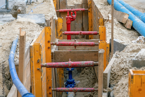 Construction site with colorful pipes and wooden supports in a trench