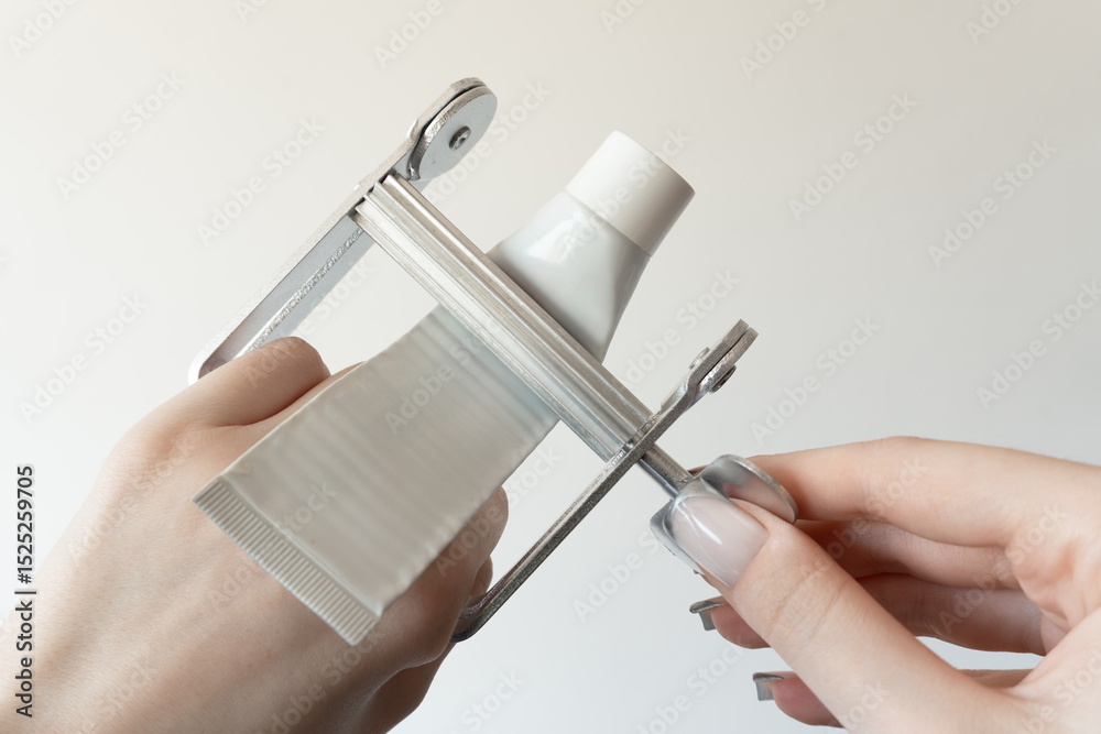 Ταπετσαρία Metal tube squeezer with a white cosmetic or toothpaste tube inserted, held in two hands on a light background