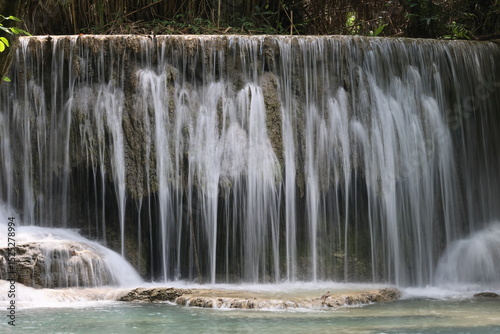 Experience the natural beauty of a flowing waterfall cascading over rocks in a lush green forest park, Kouangsi waterfall Luang Prabang
