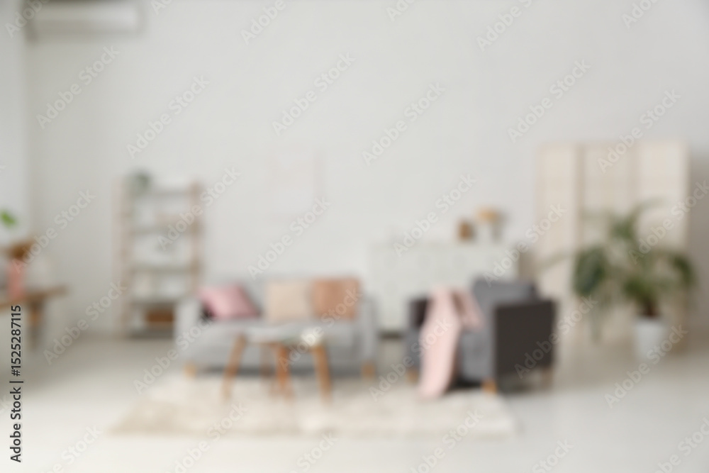 Fototapeta premium Blurred view of living room with comfortable sofa, armchair and table near white wall