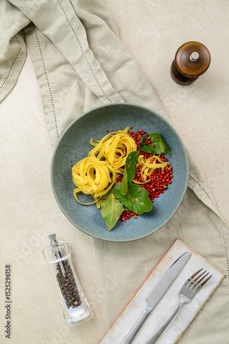 Elegant bowl of al dente pasta with vibrant red peppercorns and fresh bay leaves. Minimalistic food styling on a textured tablecloth. Perfect for culinary presentations and menu designs.
