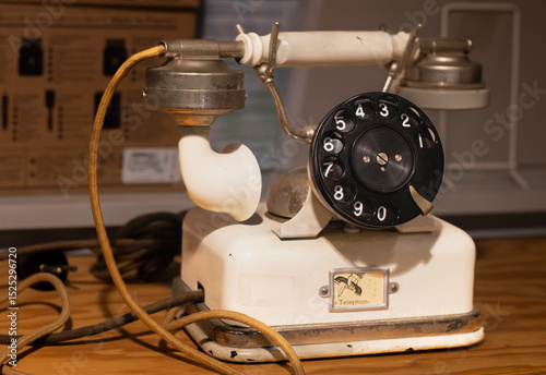 vintage rotary dial telephone with a cream-colored body, black dial, and metal earpiece. The handset rests on hooks, and the coiled cord is visibly worn and frayed from age.