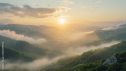 A view of a mountain range covered in fog with the sun shining through the clouds at sunrise