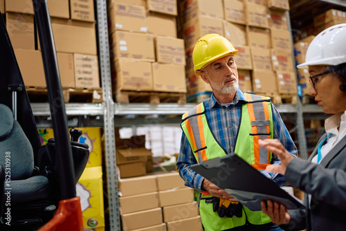 Warehouse foreman talking to female manager in storage compartment.