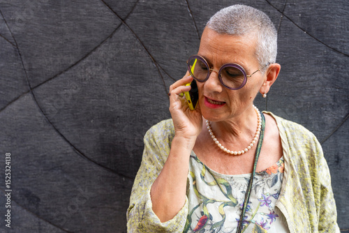 beautiful mature woman with shaved gray hair talking on cell phone in front of black wall