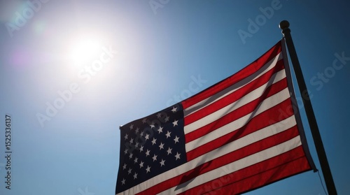 US flag flying on a pole backlit by the sun against a clear blue sky