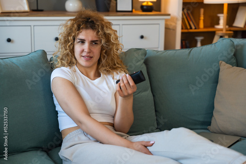 Young woman sitting on couch at home holding remote control, shocked and heartbroken while watching heartbreaking animal cruelty footage on television, emotionally affected by disturbing scenes