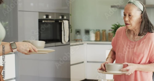 After finishing soup Asian mother and daughter carrying trays and washing dishes at kitchen island