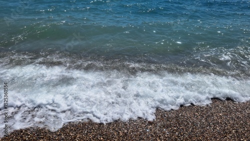 Fototapeta Naklejka Na Ścianę i Meble -  Tranquil wave washing the pebbled shore on a sunny day in Turkey