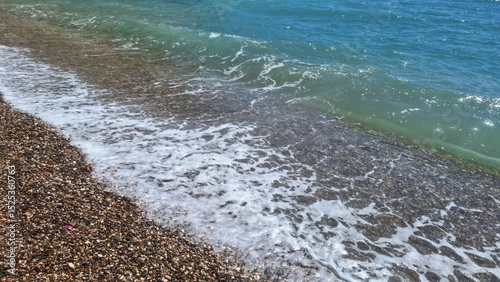 Fototapeta Naklejka Na Ścianę i Meble -  Tranquil wave washing the pebbled shore on a sunny day in Turkey