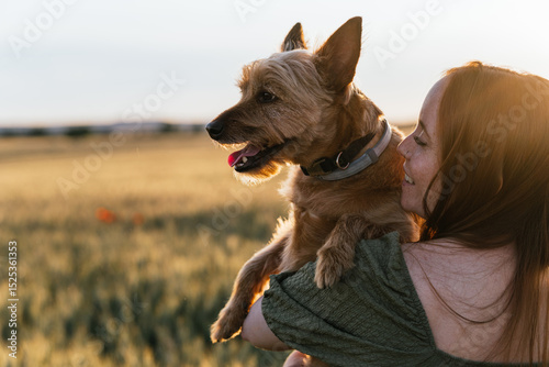 Smiling woman holding her happy dog in a wheat field at sunset