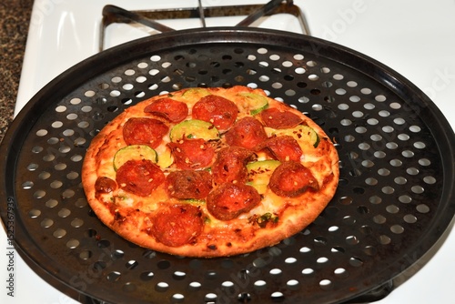 A delicious personal pizza, bubbling with melted cheese, crispy pepperoni, and fresh zucchini, resting on a perforated pizza pan.