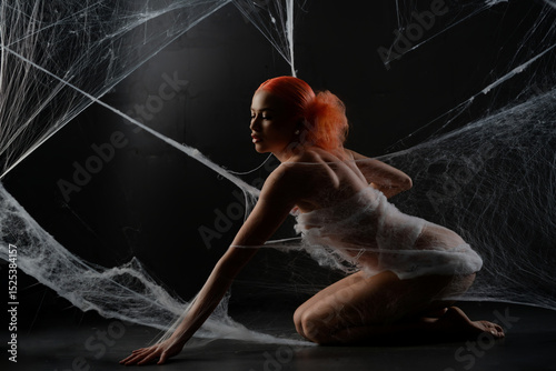 Red-haired woman trapped in a delicate web of white strands in dark setting