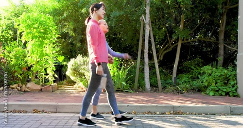 Asian Chinese mother and daughter strolling on walkway drinking from water bottle and holding hands
