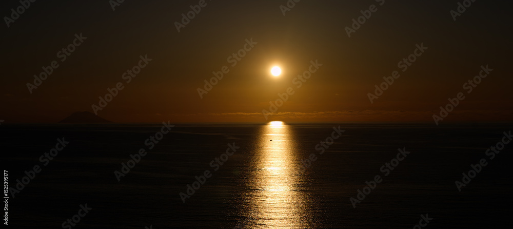 Obraz premium Sun setting over the Tyrrhenian Sea, with Stromboli Volcano visible in the distance, near Tropea, Calabria, Italy