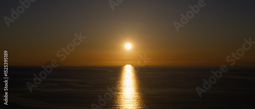 Orange sunset over Tyrrhenian Sea with Stromboli volcano silhouette and sun reflecting on water surface