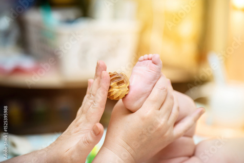 Mother giving her baby a gentle foot massage using a carved juniper wood ball, showcasing natural parenting and bonding