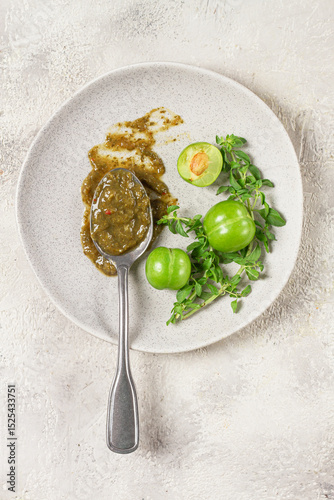 a spoon with tkemali sauce, on a plate, with cherry plum and mint, top view, no people,