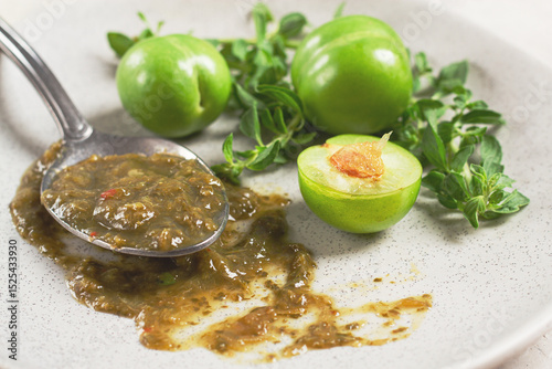 a spoon with tkemali sauce, on a plate, with cherry plum and mint, top view, no people,