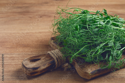 Fresh pea shoots arranged on a rustic wooden cutting board with natural textures and soft lighting in a kitchen setting