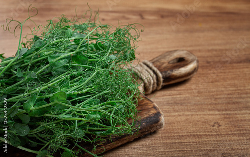 Fresh green pea sprouts piled on a rustic wooden cutting board with natural light illuminating the details