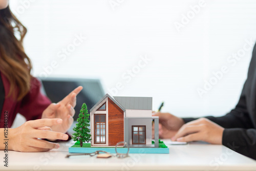 Inside a real estate office a real estate agent is using a house mockup to present the design and promotions that the client will receive when they sign sales contract. Real estate investment concept