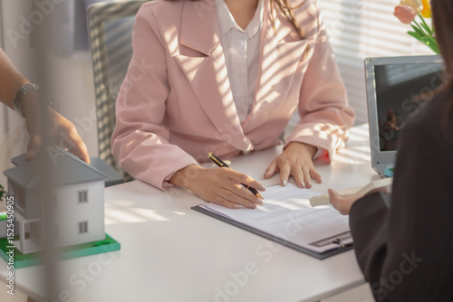 Real estate agent is in the office with the customer to prepare the documents for the real estate sale. The customer signs the sales contract before handing over the property to the customer.