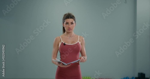 sporty girl announcer confidently speaks into the camera while holding a script in an indoor fitness area. She prepares to share insights about the upcoming activities and athletes.