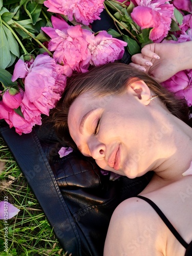 Happy smiling young woman in summer outdoors in a field with pink peony flowers enjoying life in a moment at sunset
