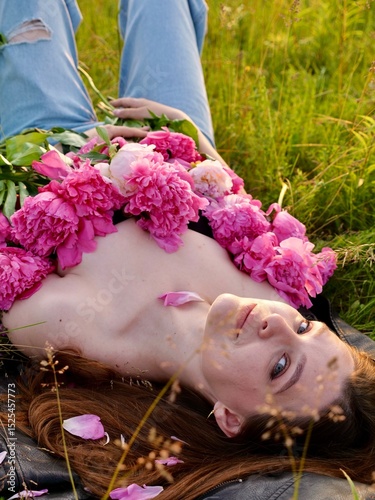 Happy smiling young woman in summer outdoors in a field with pink peony flowers enjoying life in a moment at sunset