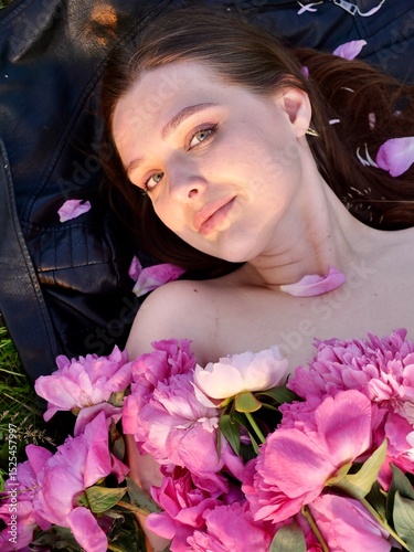 Happy smiling young woman in summer outdoors in a field with pink peony flowers enjoying life in a moment at sunset